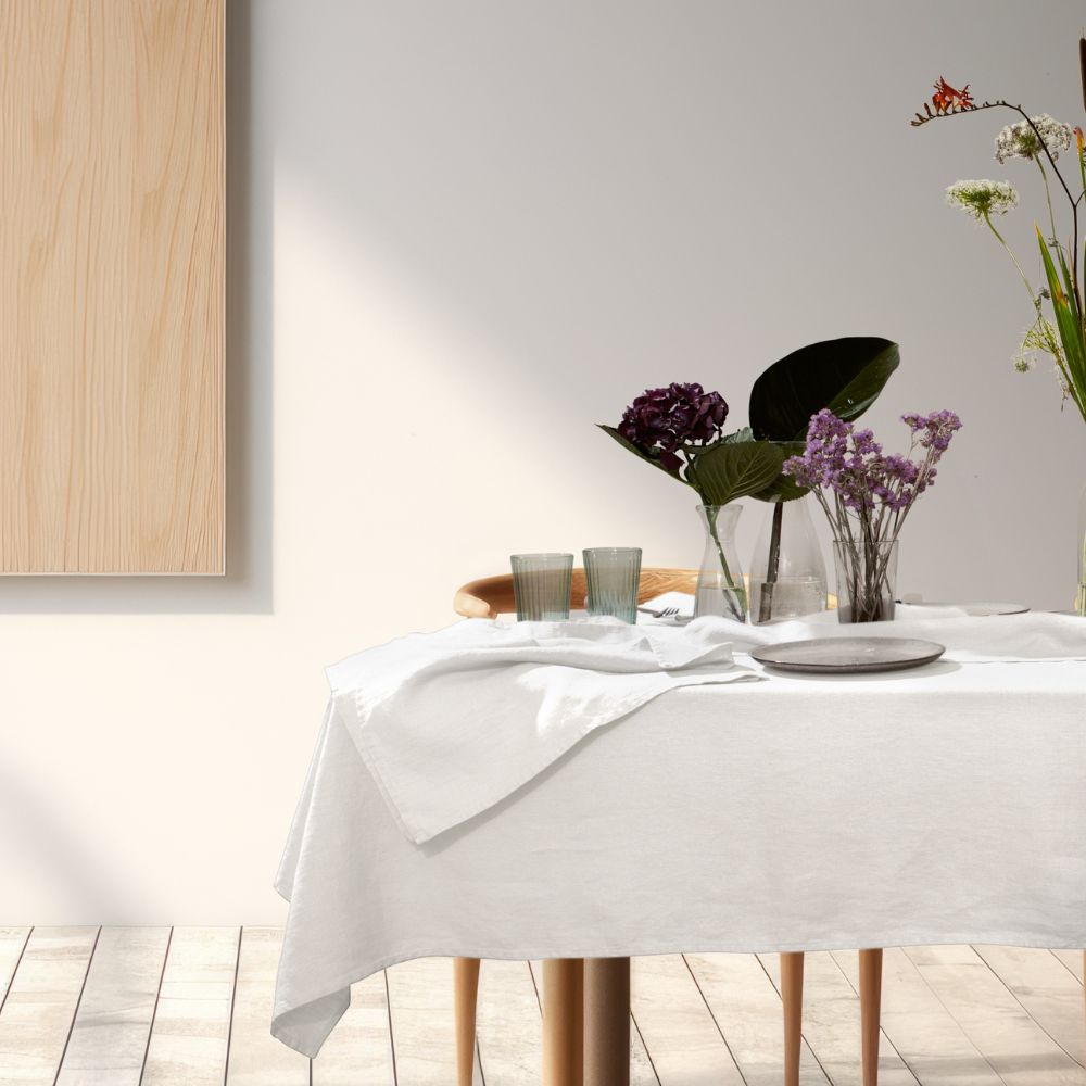 Weiße Leinen-Tischdecke mit Serviette, Weingläsern und Blumenvase auf Holztisch